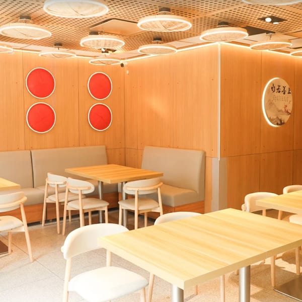 Modern restaurant interior with light wood walls, red circular decor, booth seating, and light wood tables.