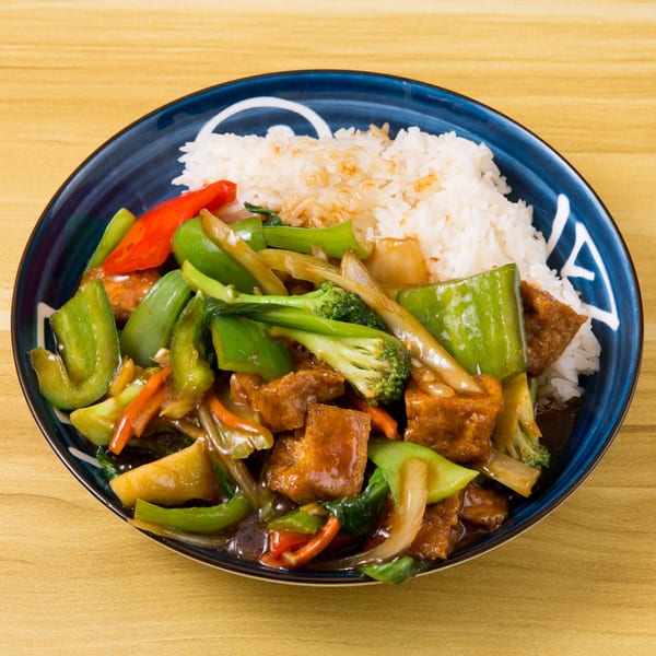 Tofu and mixed vegetables stir-fry with white rice in a blue bowl on a wooden table.