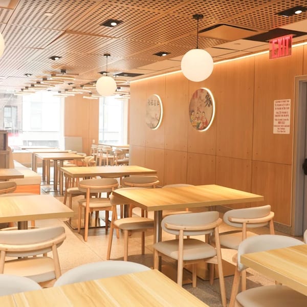 Bright, modern restaurant interior with light wood tables and chairs, circular wall art, and large windows.