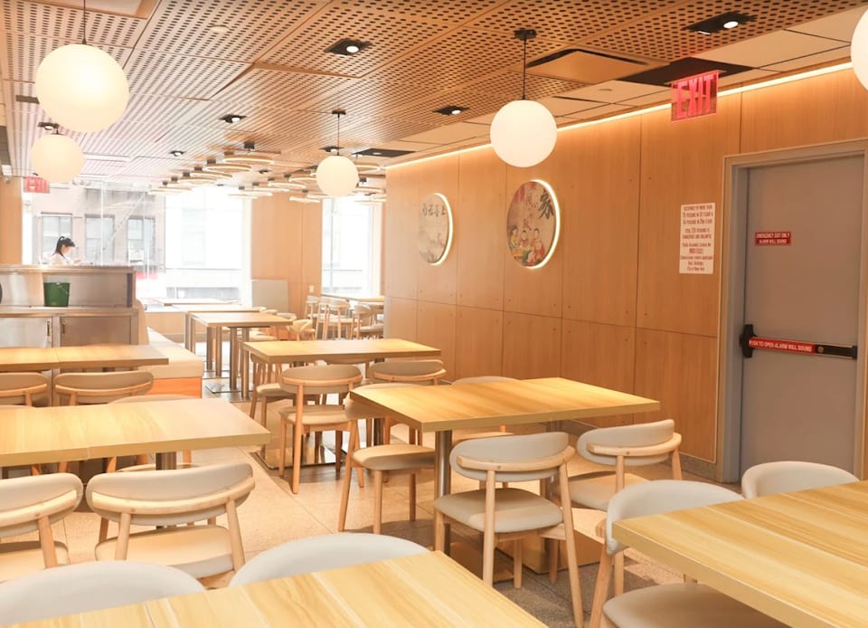 Bright, modern restaurant interior with light wood tables and chairs, circular wall art, and large windows.