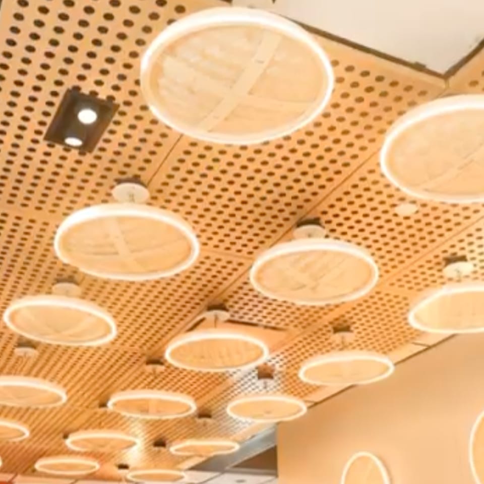 A ceiling with a wooden slatted design and circular, glowing light fixtures resembling dim sum steamers.