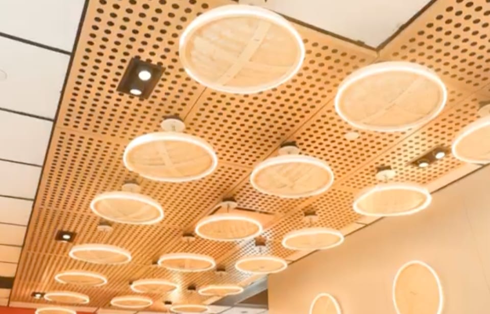 A ceiling with a wooden slatted design and circular, glowing light fixtures resembling dim sum steamers.