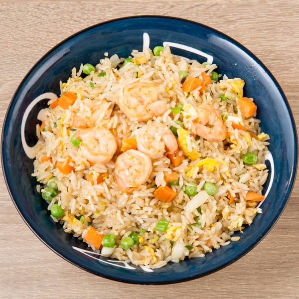 Shrimp fried rice with peas, carrots, and scrambled egg in a blue bowl on a wooden table.