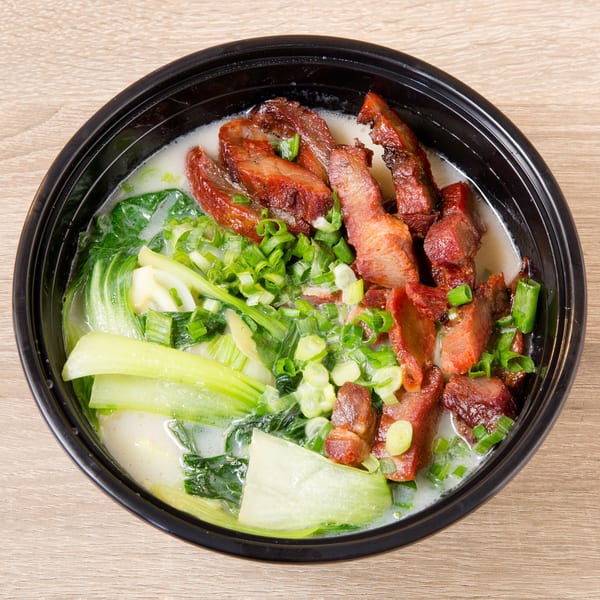 Noodle soup with bok choy, green onions, and sliced char siu pork in a black bowl.