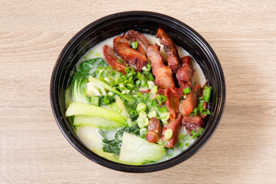 Noodle soup with bok choy, green onions, and sliced char siu pork in a black bowl.