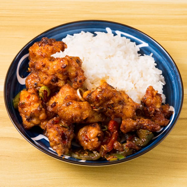 A blue bowl filled with orange chicken, white rice, and stir-fried vegetables on a wooden table.