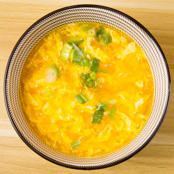 Overhead view of a bowl of golden egg drop soup garnished with chopped green onions.