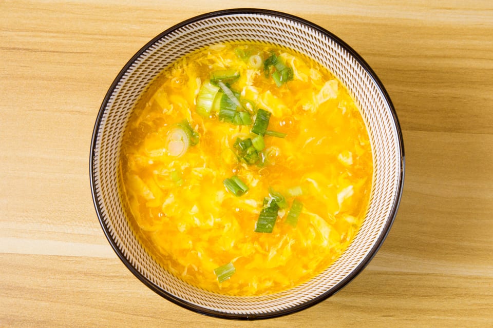 Overhead view of a bowl of golden egg drop soup garnished with chopped green onions.